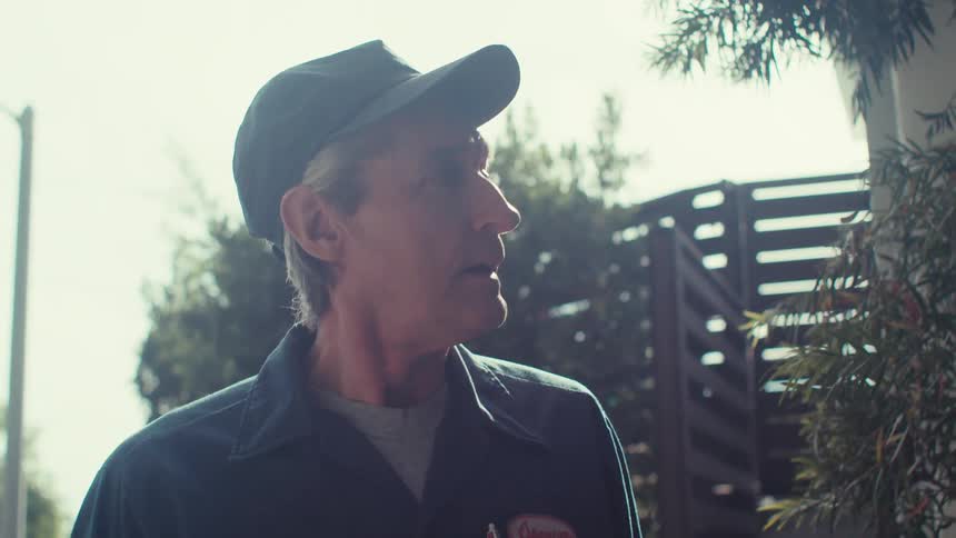 A service professional wearing a blue uniform and a cap enters a home from the backyard