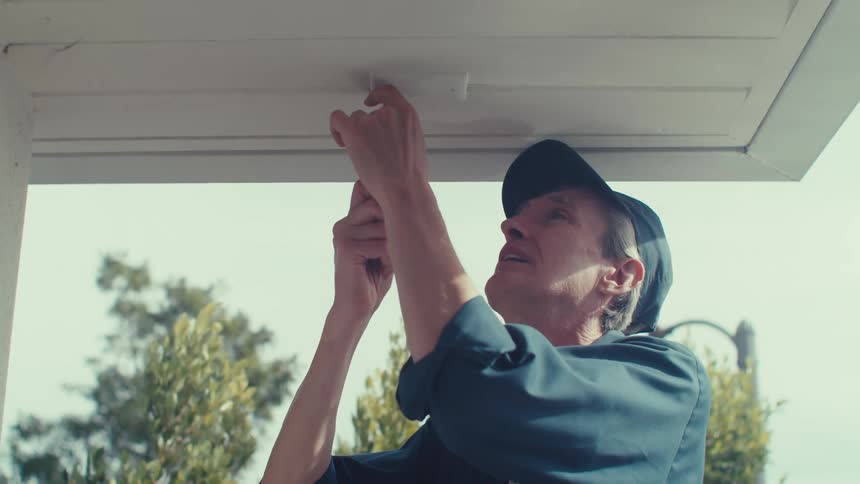 A man in a cap and blue clothes is screwing something into a white garage door that is open upwards