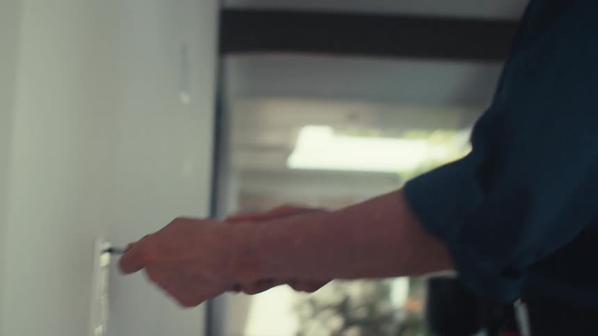 A person is using a screwdriver to adjust or install a light switch on a white wall in a modern welllit interior space