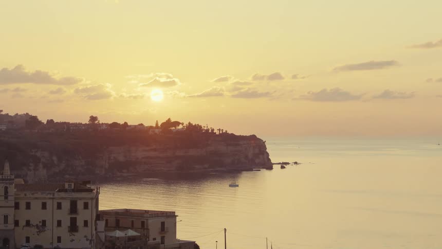 Sun sinks toward the horizon near a coastal town on a cloudy day