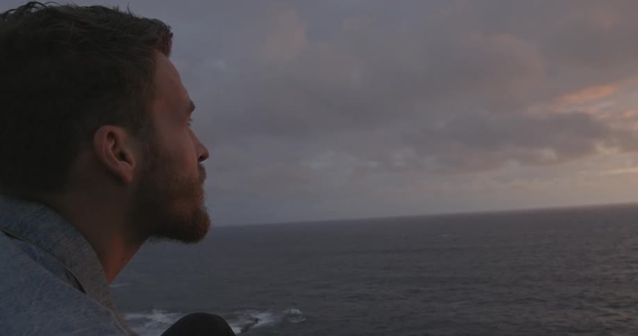 A man sits near the ocean at dusk