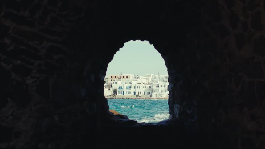 An interior view of a rock cave overlooking a sea near coastal homes