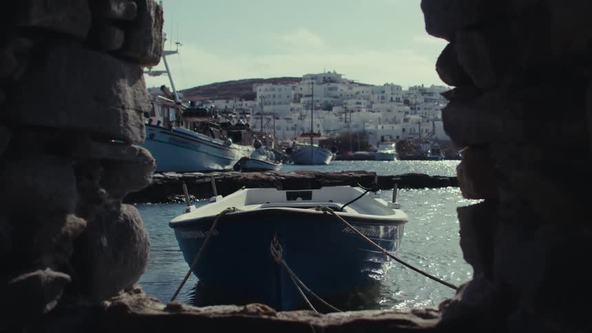 Blue boat on the sea tied by ropes with other boats and a city and a hill on the background outdoors during daytime