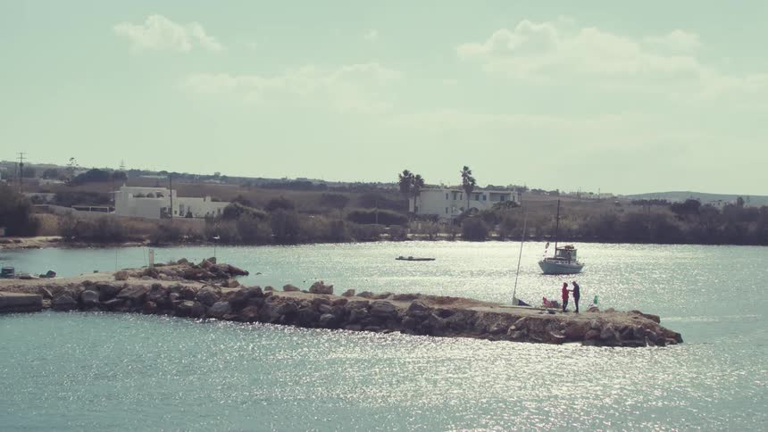 Two people on a peninsula face each other with a boat behind them