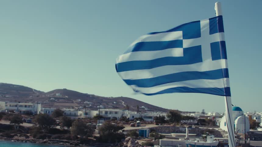 The greek flag waves proudly against a backdrop of a picturesque greek island town with a whitewashed church and boats in the harbor