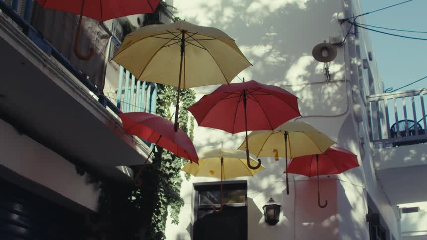 Several red and yellow umbrellas hanging from an external wire glued to the facade of a white building