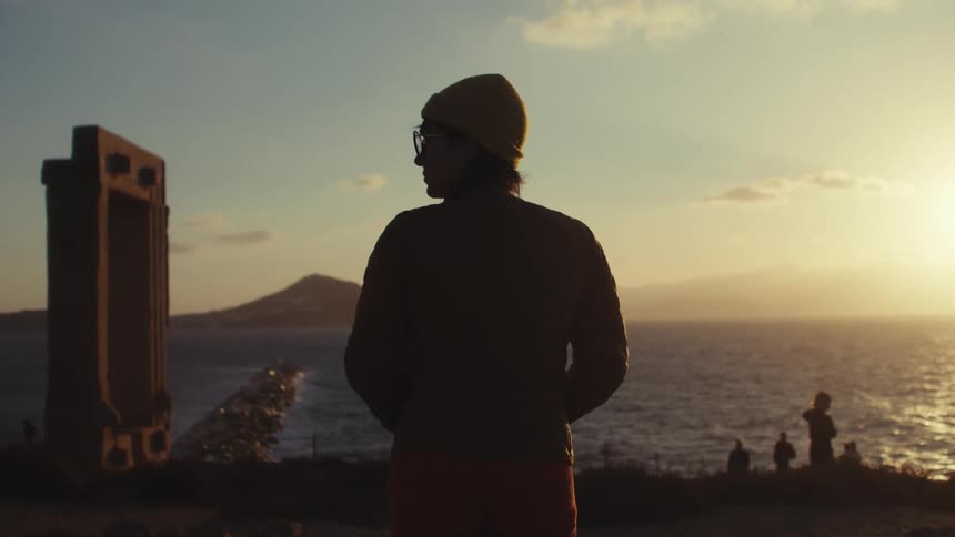 A person silhouetted against a sunset by the sea gazing at the horizon