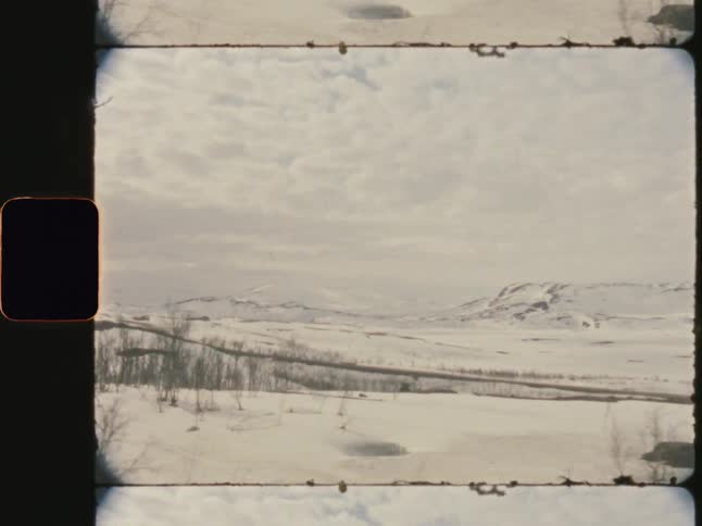 A snowy landscape with barren trees and distant hills under a cloudy sky