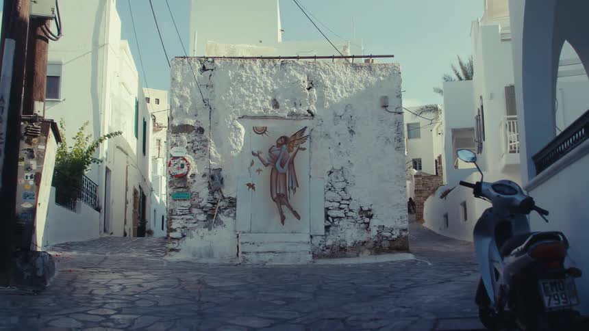 A narrow cobblestone street lined with whitewashed buildings with a painting of an angel in the center