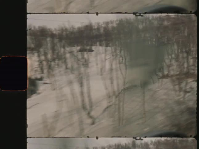 A snowy wintry landscape with hills and sparse trees visible from a moving vantage point