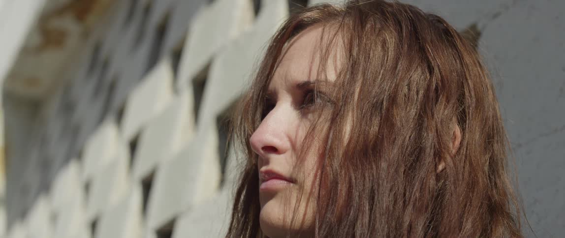 A woman stands near a wall during the daytime