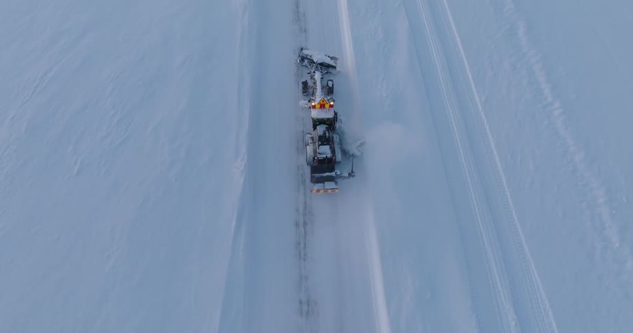 A top view of a snow plow vehicle that has a shovel in front of it and it is clearing the white snow from the road