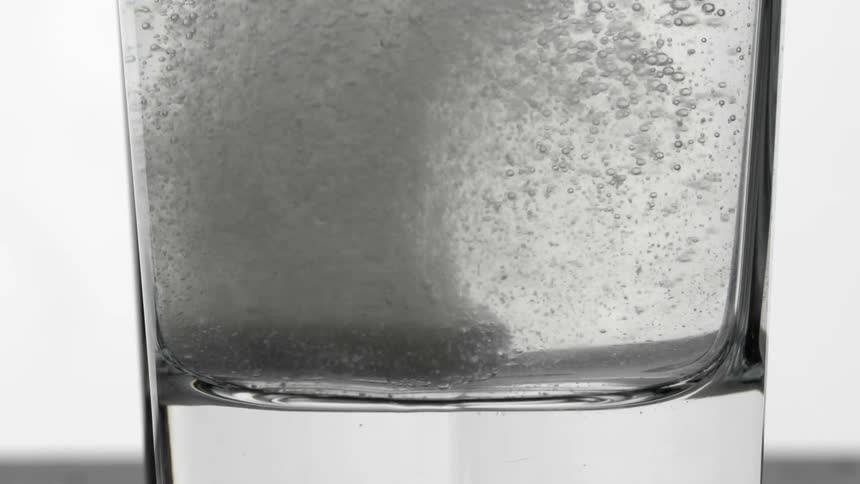Effervescent tablet dissolving on a cup of water indoors