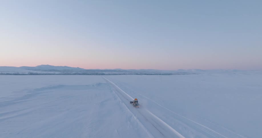 A vehicle traveling across a vast snowy landscape under a pastel sky