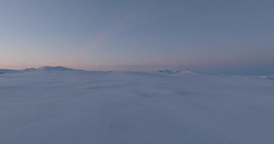 An arctic region with completely white ground covered in snow and mountains in the background on a clear sky day