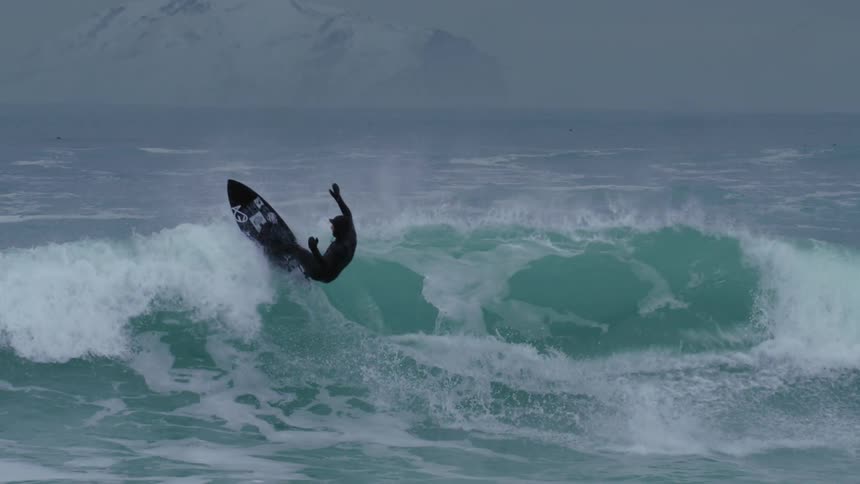 A person in a bodysuit rides a gigantic wave on a surfboard in the ocean