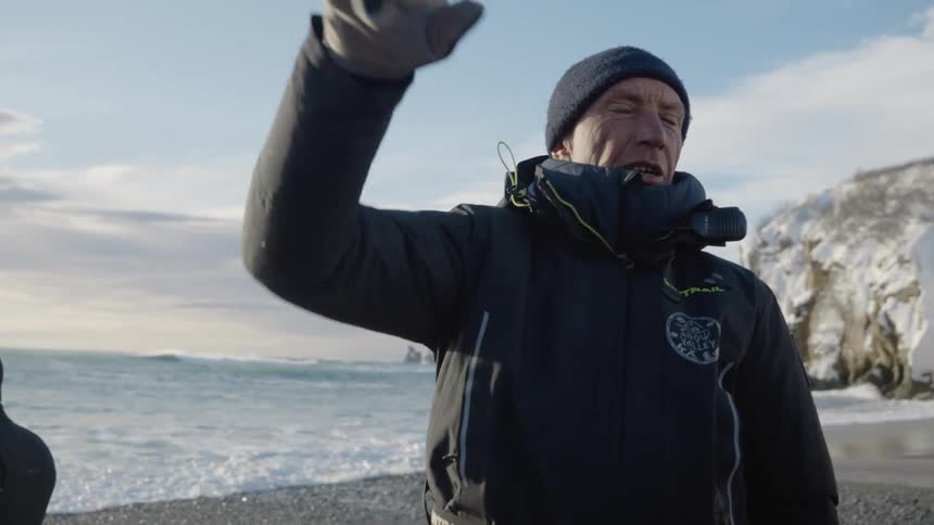 People in black wetsuits are standing on a rocky beach near an inflatable boat