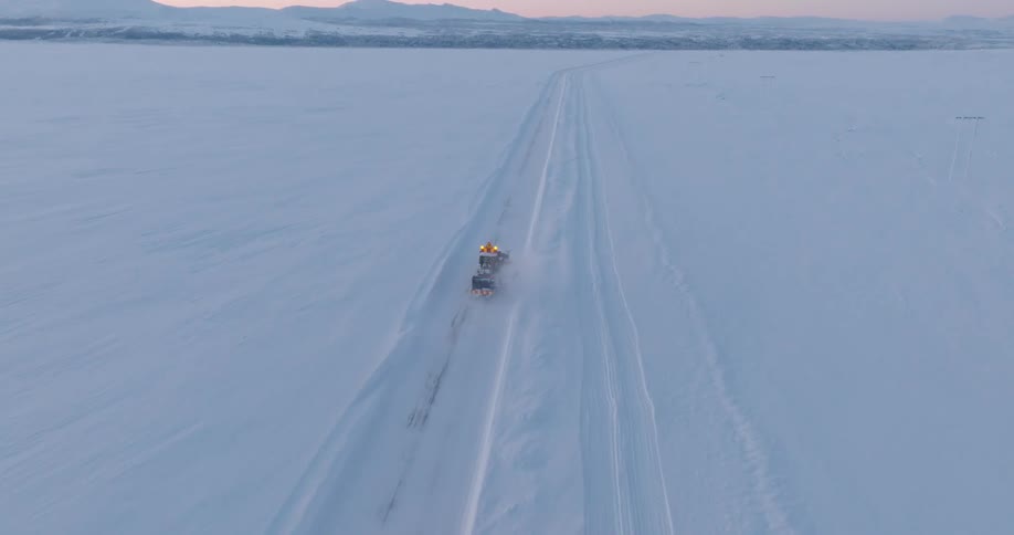 A large vehicle driving on a street in a flat area with snow on the sides