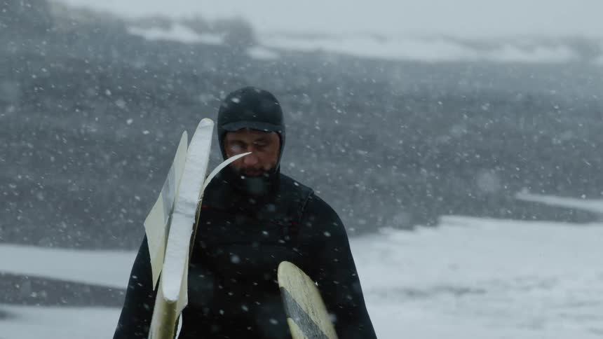 A man carries his broken surfboard in the snow