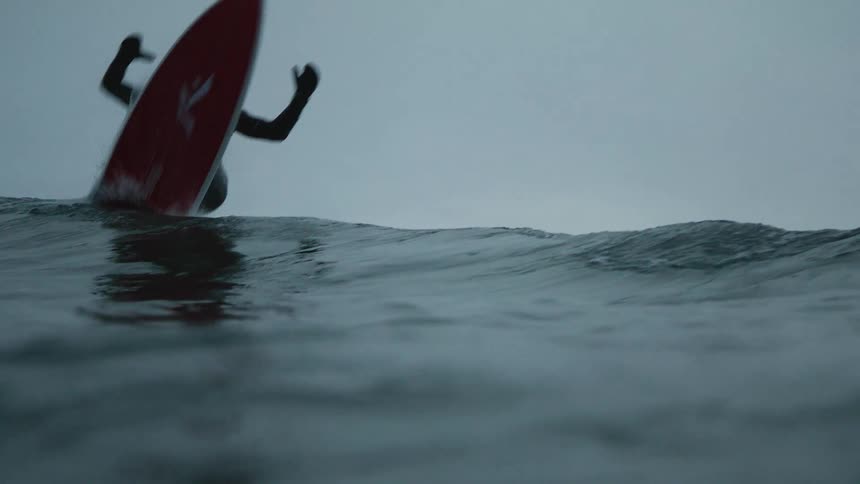 A man wearing a bodysuit rides a huge wave with his surfboard in the ocean