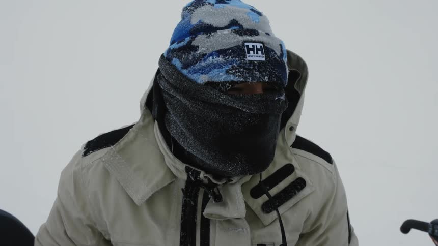 Person wearing winter outerwear that covers their face looks around while near a vehicle