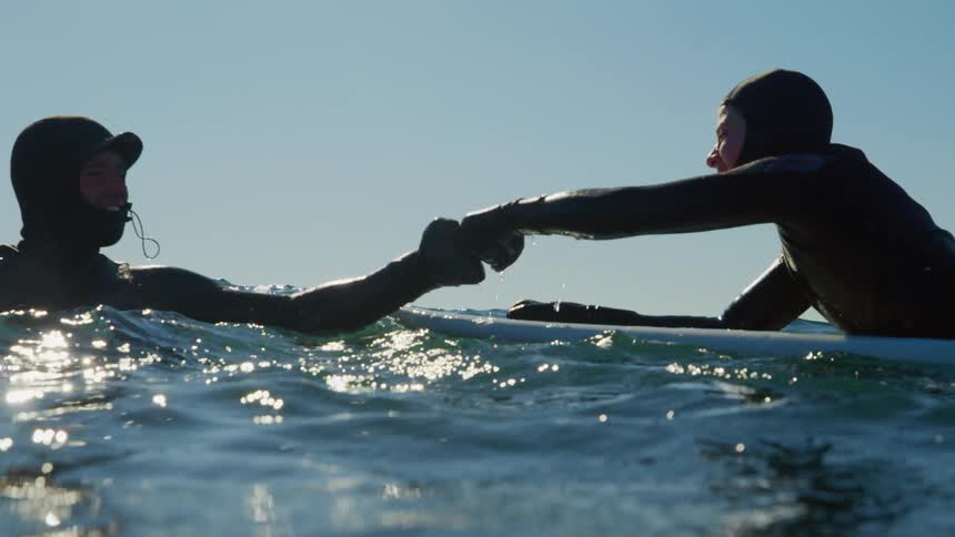 Two surfers fist bump in the water