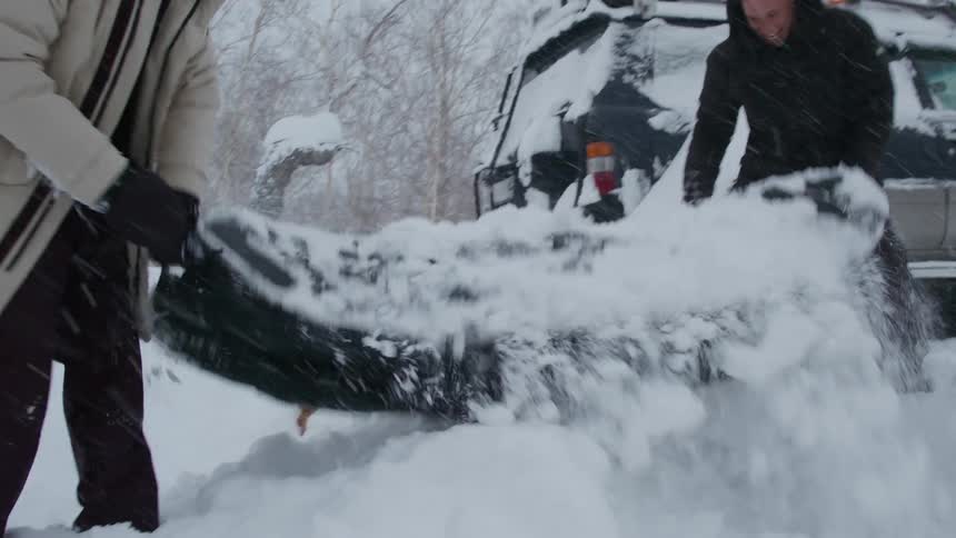 Two men shoveling snow from a long black suitcase