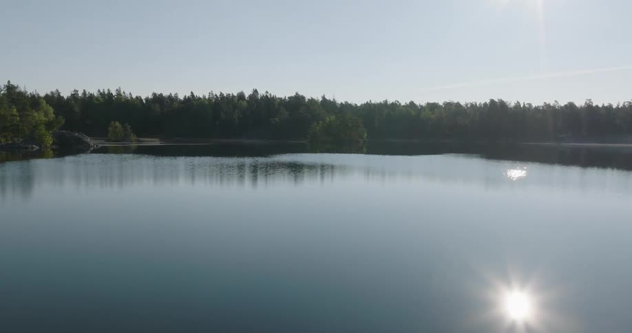 A tranquil lake reflects a line of trees under a bright sun in a calm serene setting