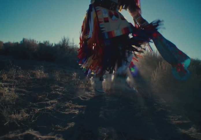 A person in colorful loose clothing is dancing on top of fine sand