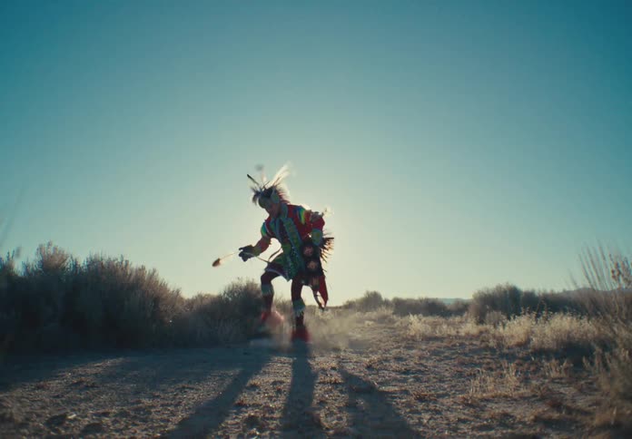 Person in native american costume dancing in a natural setting with the sun in the background