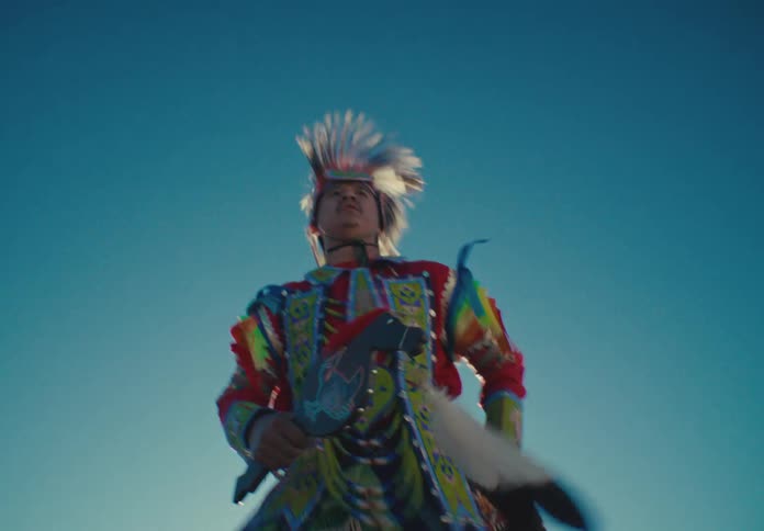 A native american dancer in vibrant regalia performing with eagle feathers against a clear blue sky