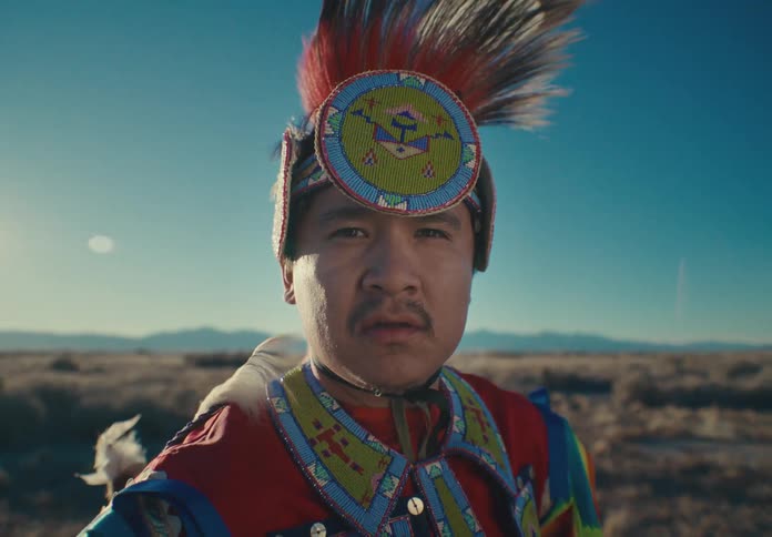 Man wears traditional native american attire while standing on a plain on a windy day