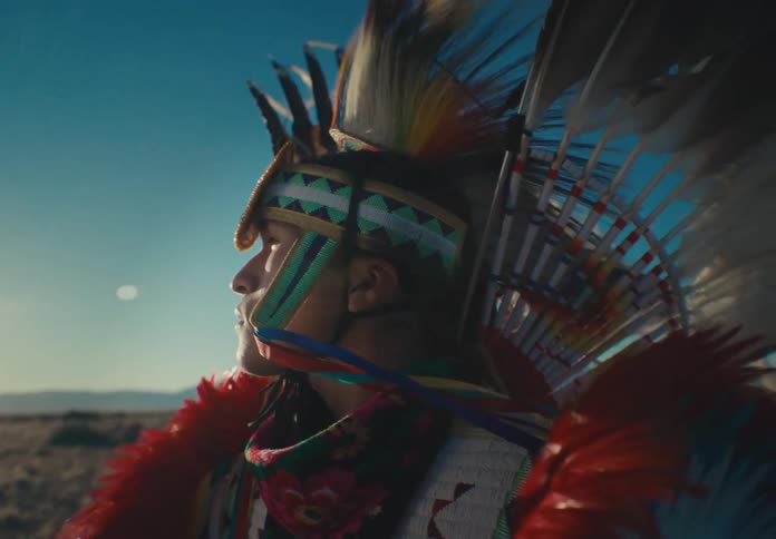 Portrait of a young tribal man in a native american feathered garment stands in a field during daytime