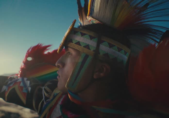 Man wearing native american attire performs in a field on a windy day