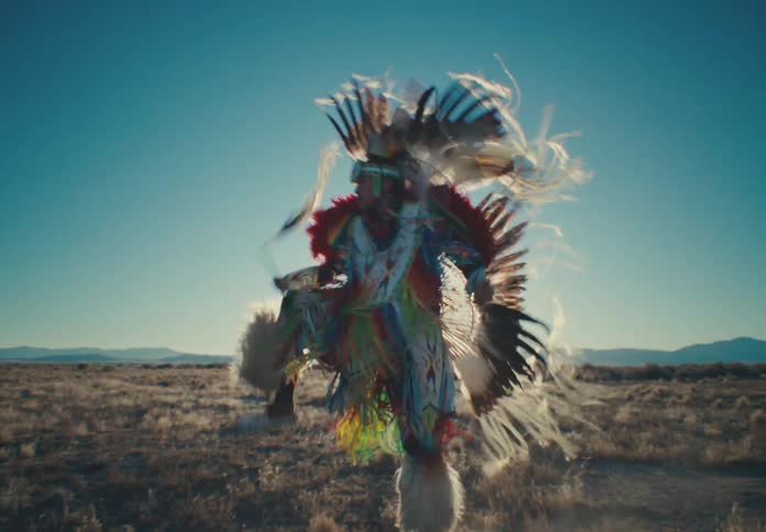 Male dancer wearing traditional native american attire performs a dance in a field on a sunny day