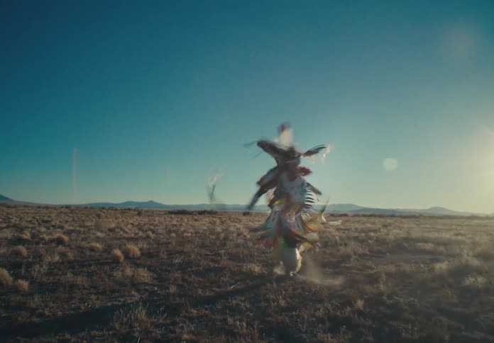 A native american man dances in colorful clothing in a grassland
