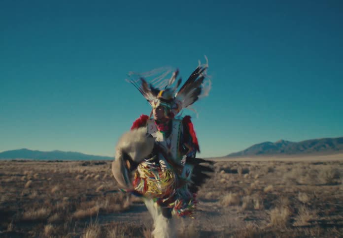 A dancer in traditional regalia performing energetically in a desert landscape
