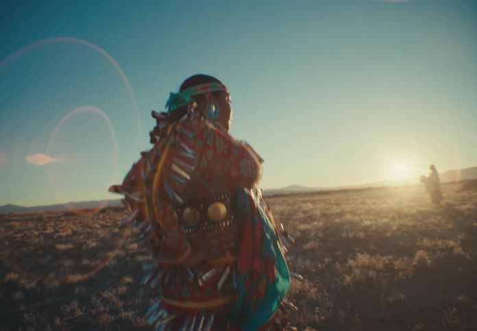 Native american woman dancing in traditional dress in a field with another person in the background