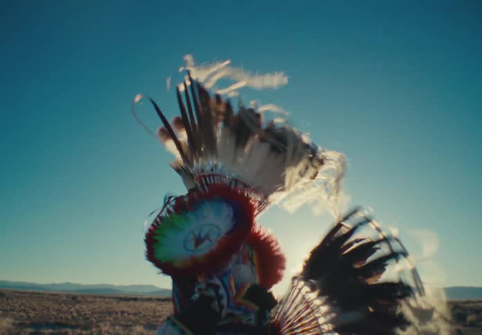Person in traditional native american clothing dancing in a field with sparse vegetation