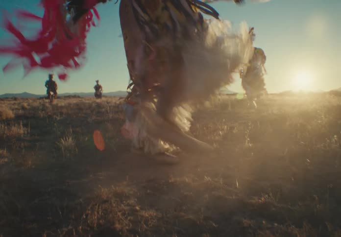 A group of dancers performing on a dusty field as the sun sets