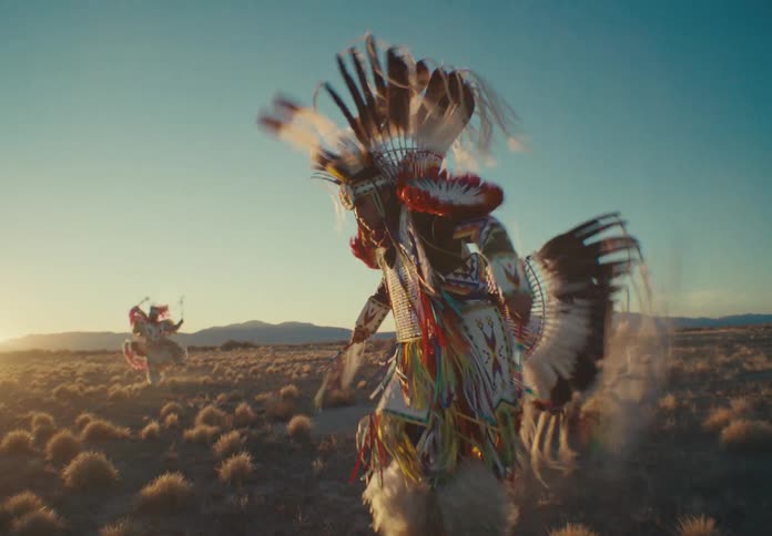 Group of people dancing in a desert field wearing traditional native american clothing