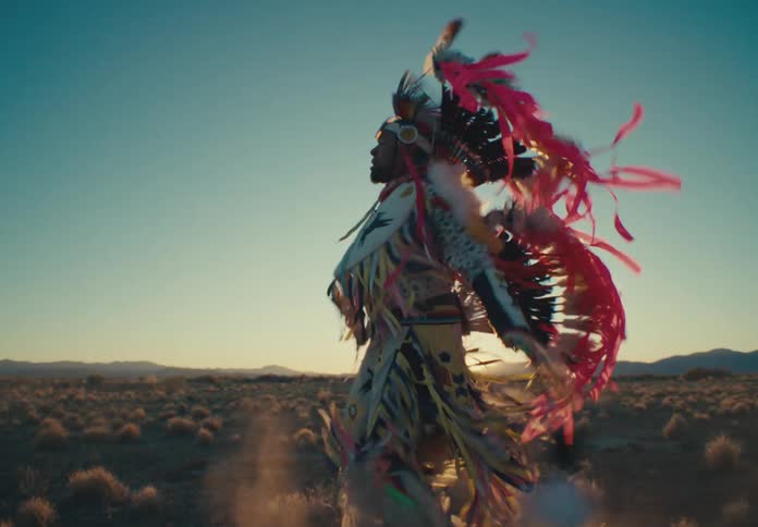 Man in traditional native american clothing dancing in a desert environment with sparse vegetation