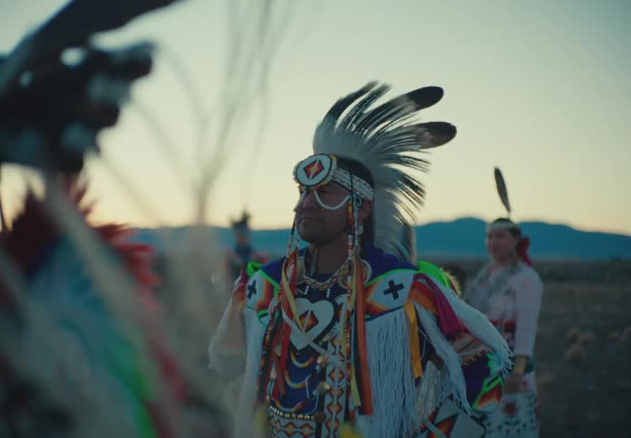 Group of people in native american attire in a field with mountains in the background