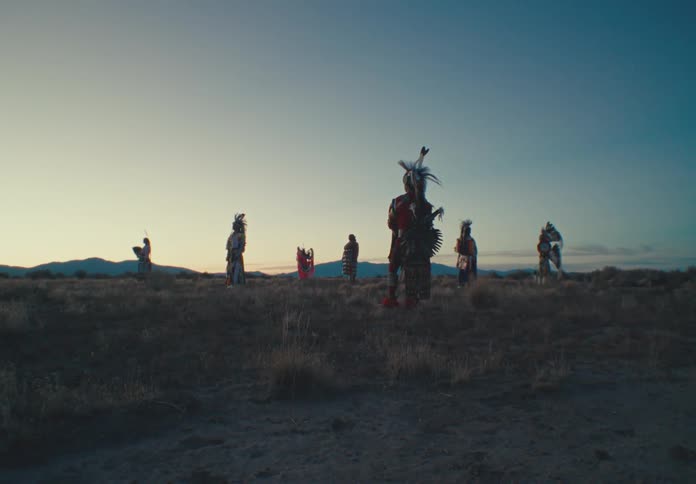 People wearing native american attire stand in a field after dusk