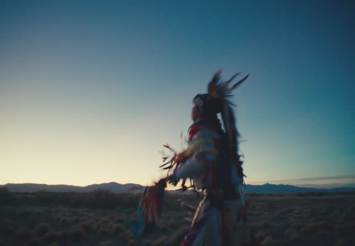 A person wearing colorful feathered clothing doing small jumps in a desert region