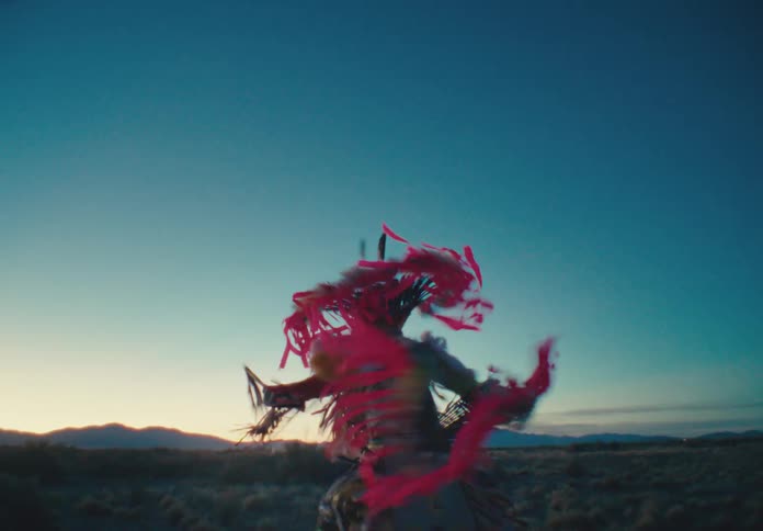 Male dancer wearing native american attire dances in a field near sunrise