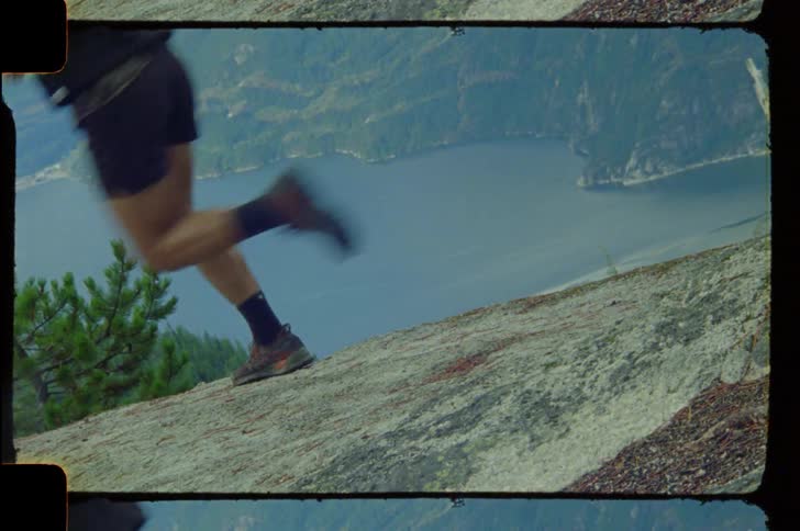 Legs of a person running on a rock and a mountain overlooking a lake in the background