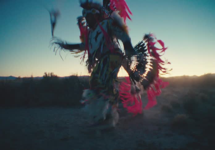 A person in white and red feathered clothing performing a ritualistic dance in a desert