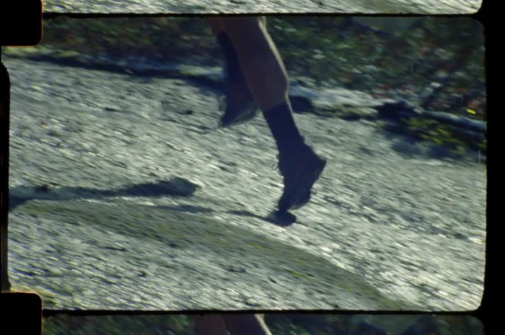 A woman shown from the waist down jogs up a grassy hill