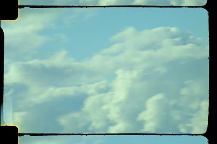 A long shot of fluffy white clouds drifting across a pale blue sky is shown